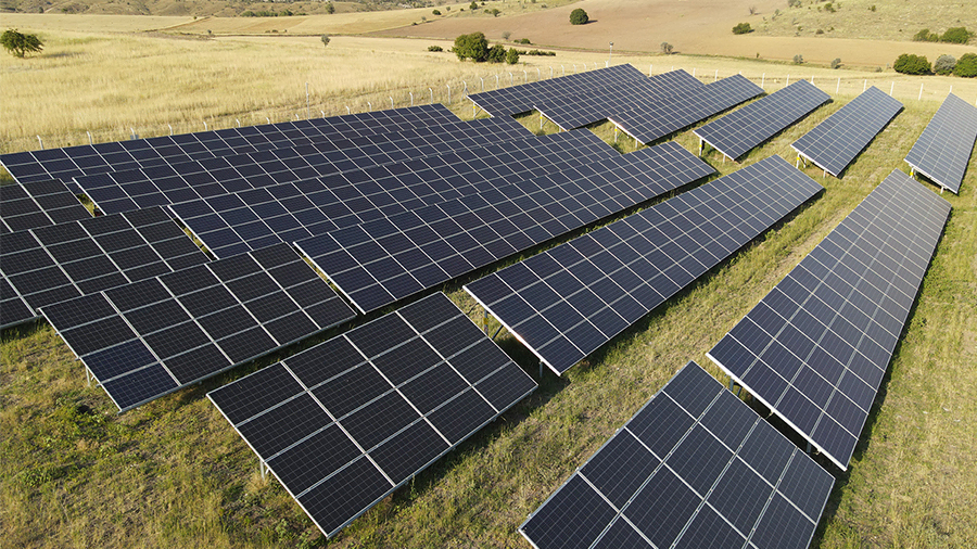 Güneş enerjisi sistemleri kurulmuş bir tarlada, panellerin ve çevresel yeşilliklerin gösterildiği fotoğraf.